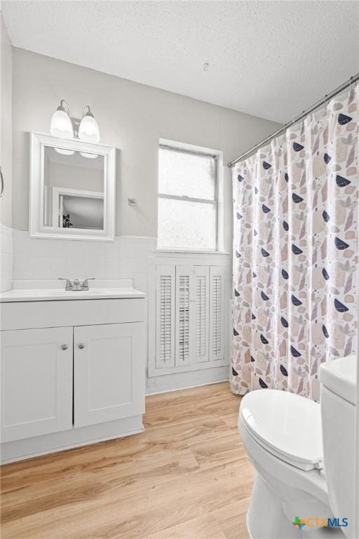 full bathroom with tile walls, toilet, wainscoting, a textured ceiling, and wood finished floors