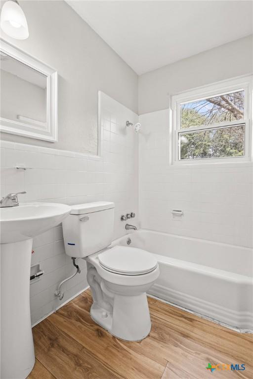 bathroom featuring toilet,  shower combination, tile walls, and wood finished floors