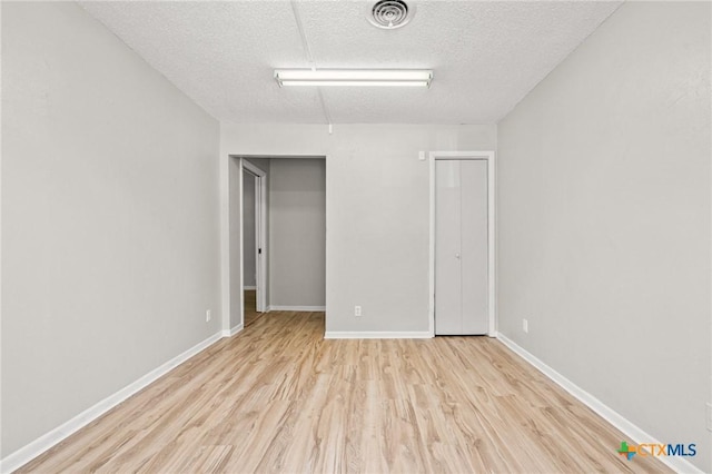 unfurnished room with baseboards, a textured ceiling, visible vents, and wood finished floors