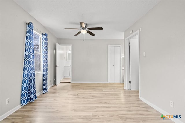 empty room featuring a ceiling fan, baseboards, a textured ceiling, and light wood finished floors