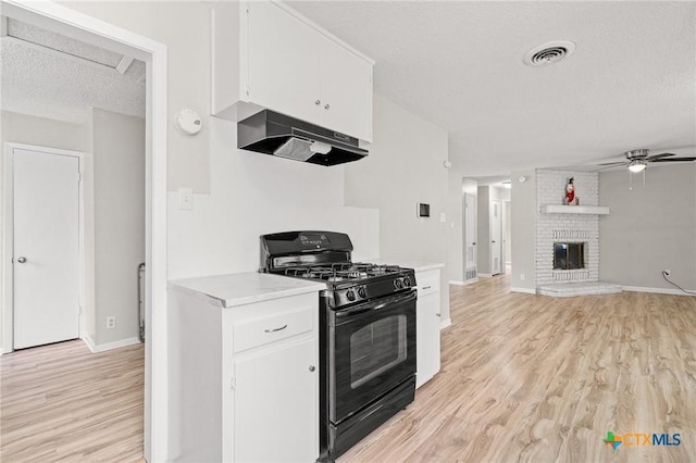 kitchen featuring black gas range, light countertops, under cabinet range hood, a fireplace, and white cabinetry