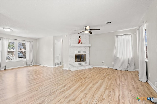 unfurnished living room with baseboards, visible vents, wood finished floors, a textured ceiling, and a brick fireplace