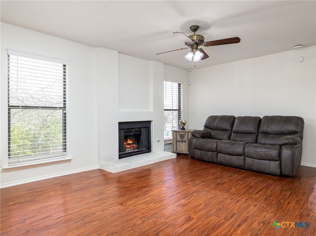 living room featuring a brick fireplace, a ceiling fan, baseboards, and wood finished floors