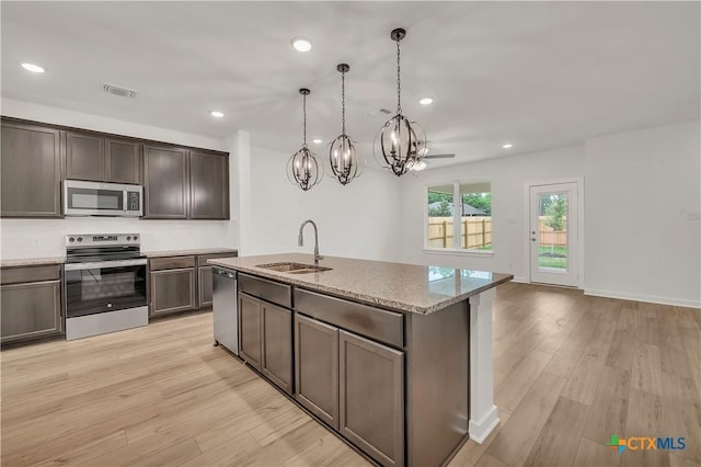 kitchen with a sink, visible vents, light wood-style floors, light stone countertops, and appliances with stainless steel finishes