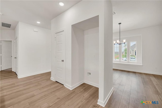 hallway with light wood-type flooring, visible vents, baseboards, and a notable chandelier
