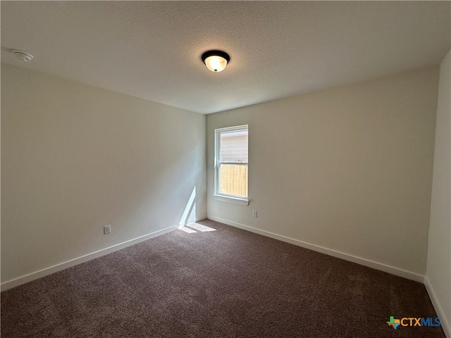 spare room featuring a textured ceiling, baseboards, and dark colored carpet