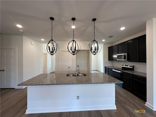 kitchen featuring a sink, appliances with stainless steel finishes, dark wood finished floors, and dark stone countertops