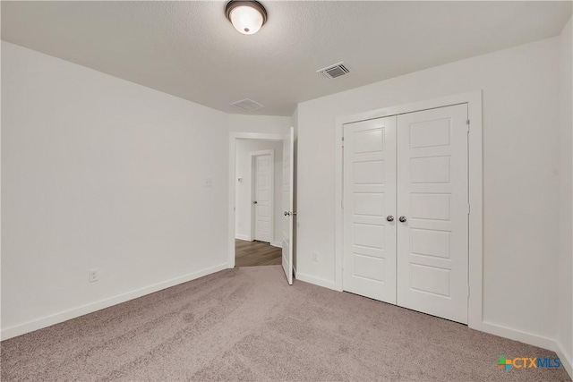 unfurnished bedroom featuring a textured ceiling, a closet, baseboards, carpet flooring, and visible vents