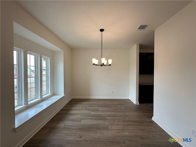 unfurnished dining area with dark wood finished floors, baseboards, visible vents, and a chandelier