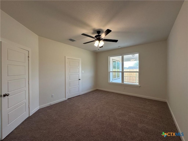 unfurnished room with a ceiling fan, baseboards, visible vents, and dark carpet