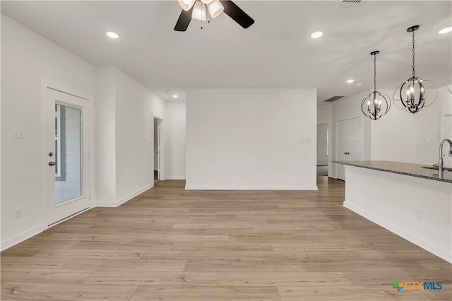 unfurnished living room with ceiling fan with notable chandelier, baseboards, a sink, and recessed lighting