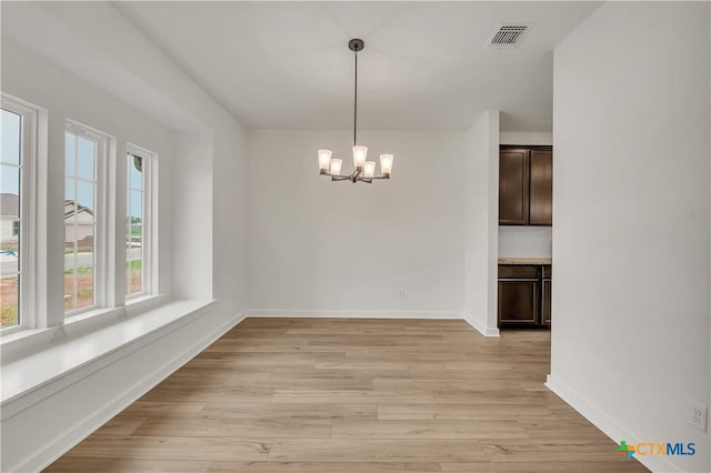 unfurnished dining area with baseboards, visible vents, an inviting chandelier, and light wood-style floors