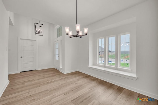 unfurnished dining area with light wood finished floors, baseboards, and a notable chandelier