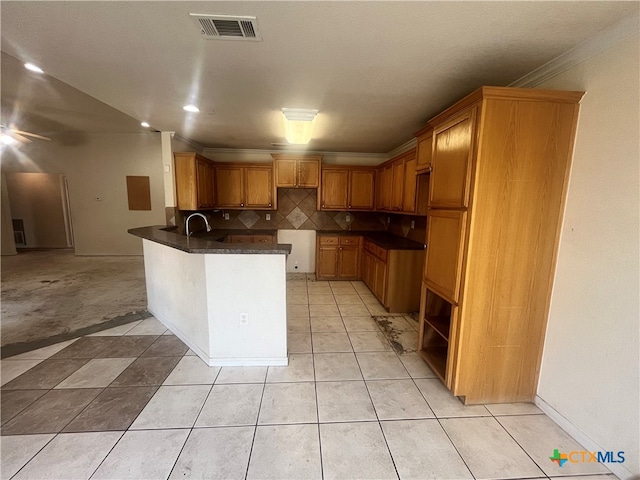 kitchen with light tile patterned flooring, crown molding, dark stone counters, decorative backsplash, and kitchen peninsula