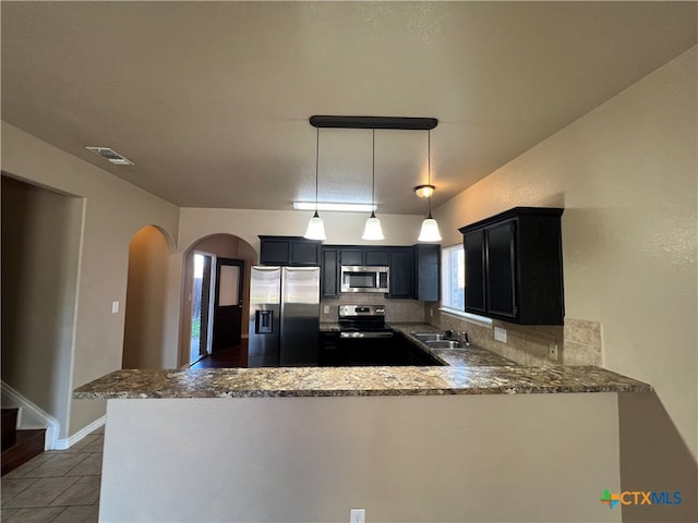 kitchen featuring pendant lighting, kitchen peninsula, decorative backsplash, and stainless steel appliances