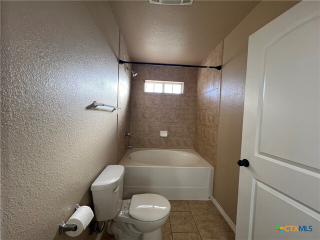 bathroom featuring toilet, tiled shower / bath, a textured ceiling, and tile patterned floors