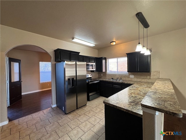 kitchen featuring stainless steel appliances, sink, kitchen peninsula, decorative light fixtures, and decorative backsplash