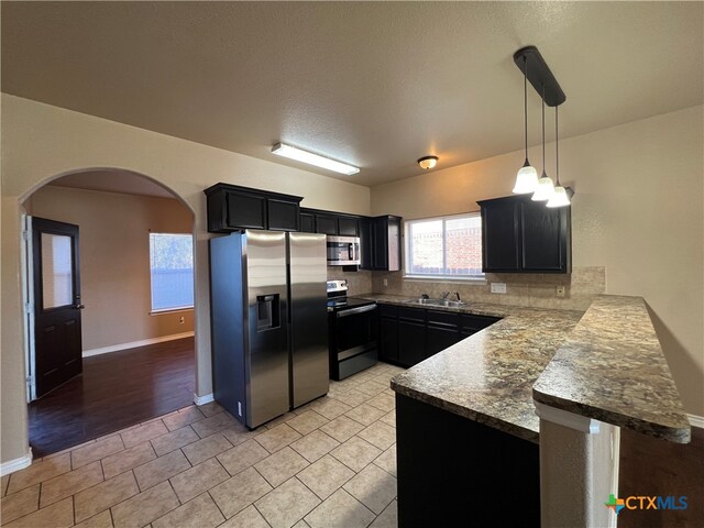 kitchen featuring stainless steel appliances, sink, kitchen peninsula, decorative light fixtures, and decorative backsplash