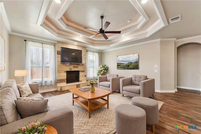 living area featuring a large fireplace, wood finished floors, visible vents, a tray ceiling, and crown molding