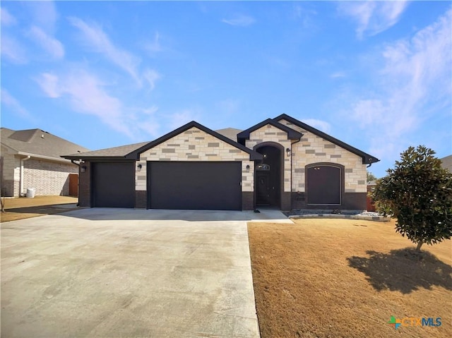 french country style house with a garage, concrete driveway, brick siding, and stone siding