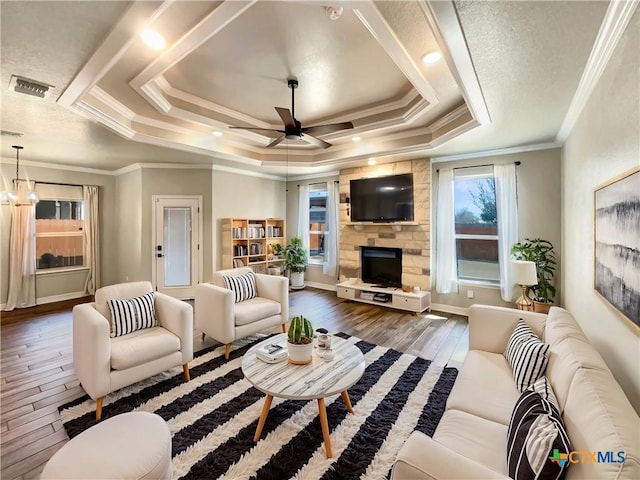 living area featuring visible vents, a raised ceiling, wood finished floors, a stone fireplace, and ceiling fan with notable chandelier