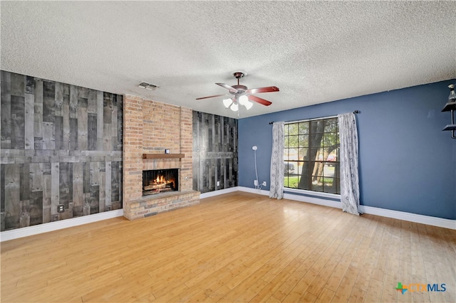 unfurnished living room featuring a brick fireplace, wood-type flooring, a textured ceiling, and ceiling fan