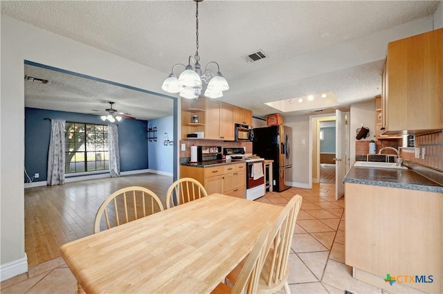 dining area with ceiling fan with notable chandelier, light hardwood / wood-style flooring, a textured ceiling, and sink