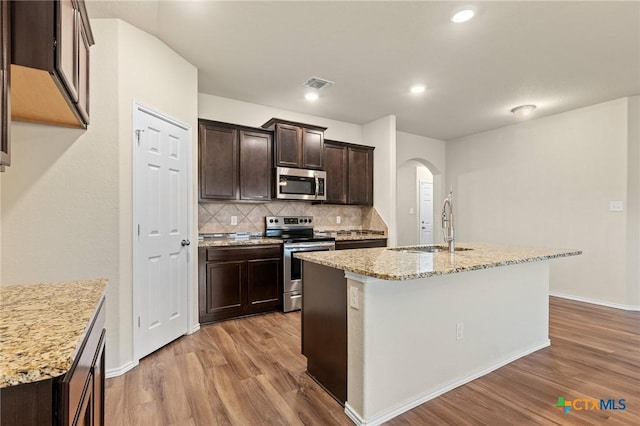 206 Danielle Dr, Killeen, TX 76542 - kitchen with stainless steel appliances, light wood-style flooring, decorative backsplash, arched walkways, and dark brown cabinetry