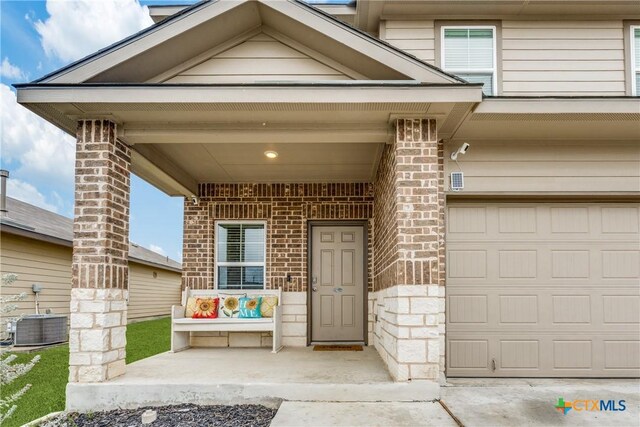 view of exterior entry with a porch, a garage, and central air condition unit