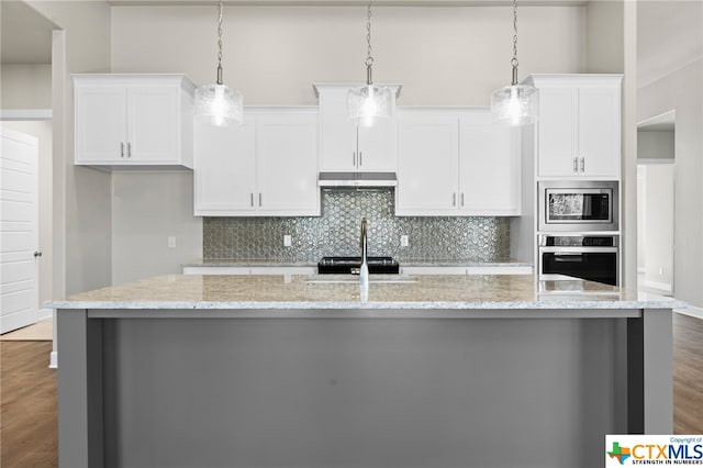 kitchen featuring light stone countertops, hanging light fixtures, a center island with sink, white cabinets, and appliances with stainless steel finishes