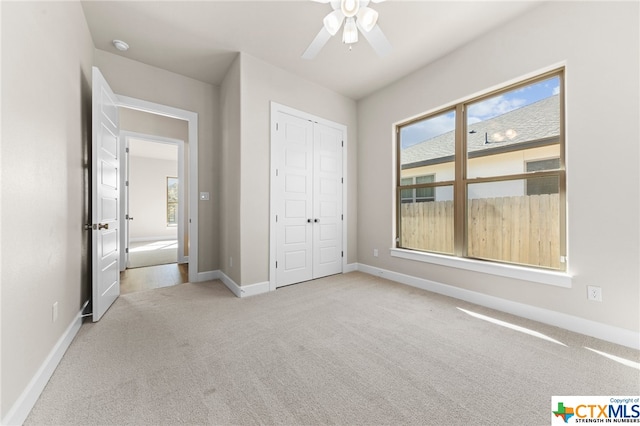 unfurnished bedroom with ceiling fan, multiple windows, light carpet, and a closet