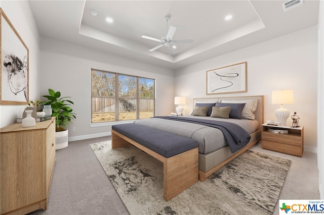 carpeted bedroom with ceiling fan and a tray ceiling