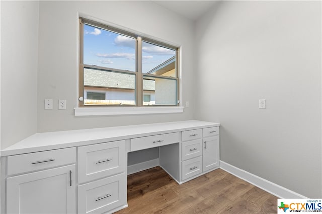 unfurnished office featuring built in desk and light hardwood / wood-style floors