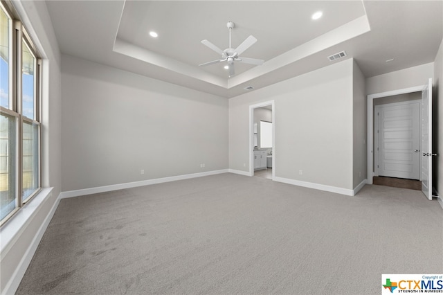 unfurnished bedroom featuring ceiling fan, light colored carpet, ensuite bathroom, and a tray ceiling