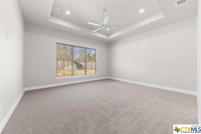 carpeted spare room with ceiling fan and a tray ceiling