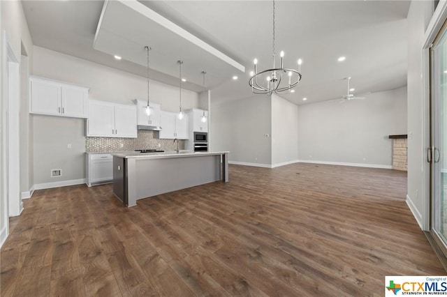 kitchen featuring decorative backsplash, ceiling fan with notable chandelier, pendant lighting, a center island with sink, and white cabinets