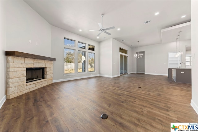 unfurnished living room featuring a fireplace, dark wood-type flooring, ceiling fan with notable chandelier, and sink