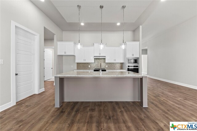 kitchen with a center island with sink, white cabinets, light stone countertops, appliances with stainless steel finishes, and tasteful backsplash