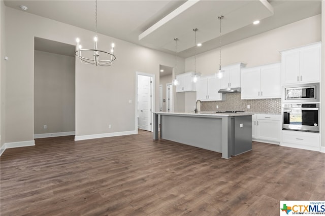 kitchen with appliances with stainless steel finishes, decorative light fixtures, white cabinetry, and a kitchen island with sink