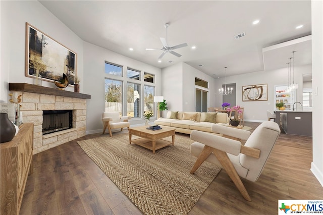 living room featuring a stone fireplace, plenty of natural light, ceiling fan with notable chandelier, and hardwood / wood-style flooring