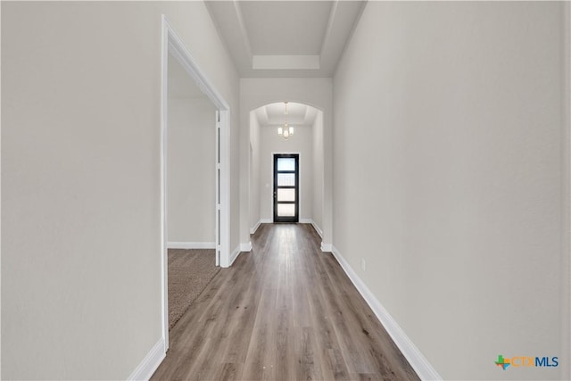 corridor featuring baseboards, arched walkways, and wood finished floors