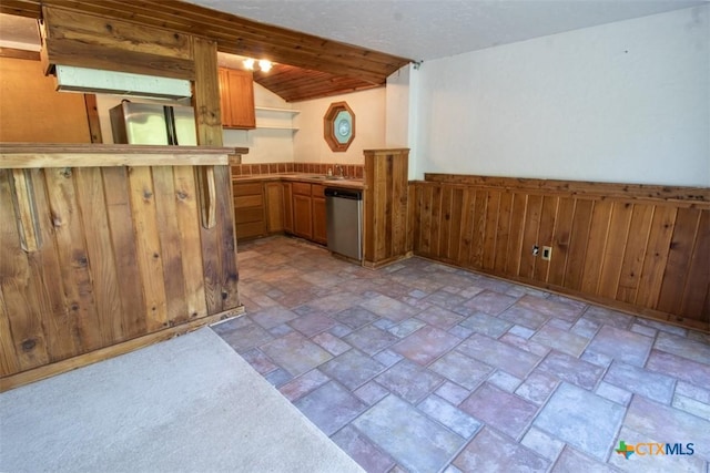 kitchen featuring stainless steel dishwasher, light stone finish floors, wainscoting, a sink, and brown cabinets
