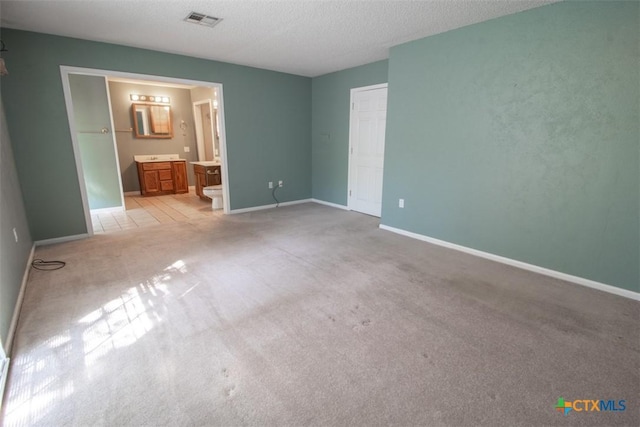 unfurnished bedroom with light colored carpet, ensuite bathroom, baseboards, and a textured ceiling