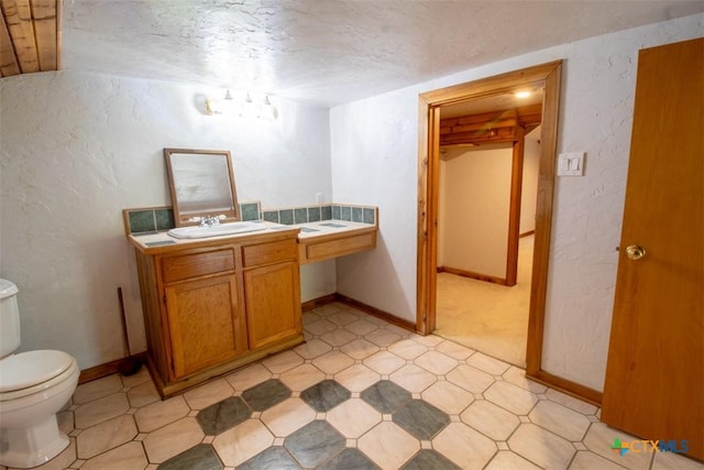 bathroom with toilet, vanity, a textured wall, tile patterned floors, and a textured ceiling