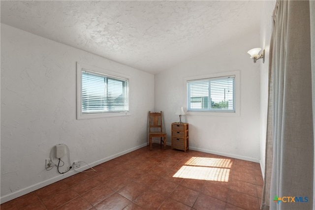 tiled empty room featuring lofted ceiling, a textured ceiling, and a wealth of natural light