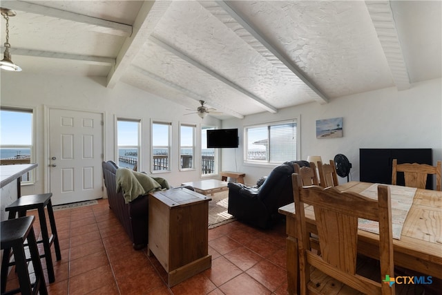 living room with dark tile patterned flooring, lofted ceiling with beams, a water view, ceiling fan, and a textured ceiling