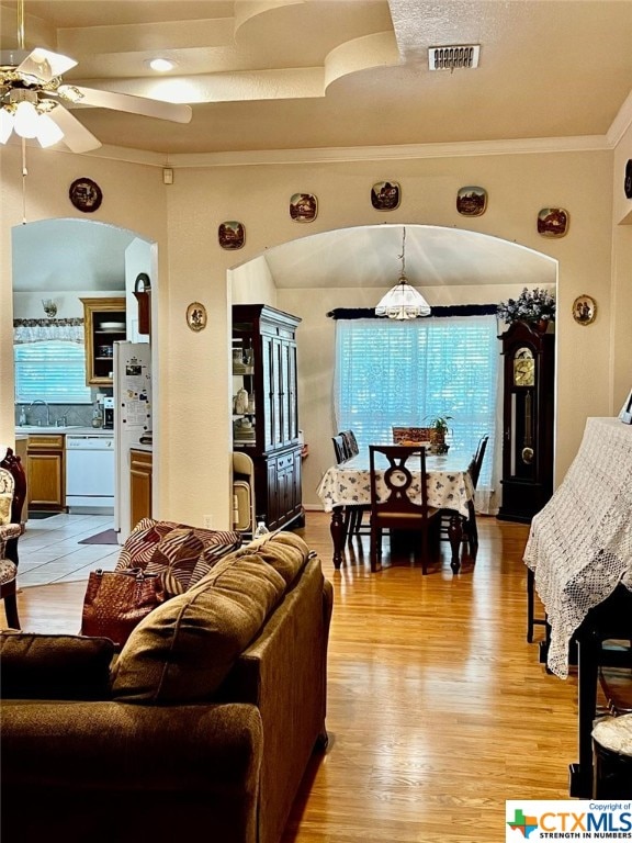 living room featuring ceiling fan, sink, ornamental molding, and light hardwood / wood-style flooring