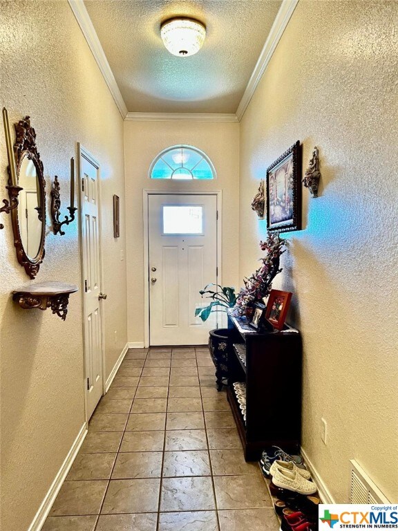 4305 Foster Ln, Killeen, TX 76549 - doorway featuring a textured ceiling, crown molding, a textured wall, light tile patterned floors, and baseboards