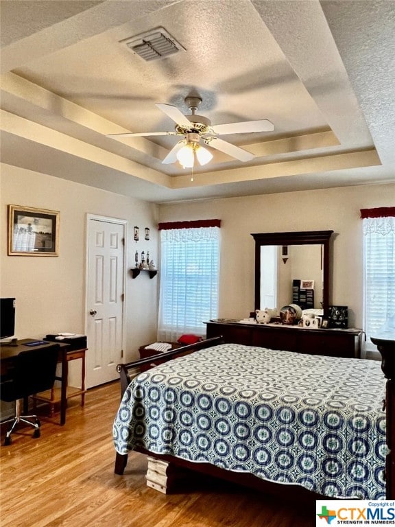 bedroom with light hardwood / wood-style flooring, multiple windows, and a raised ceiling