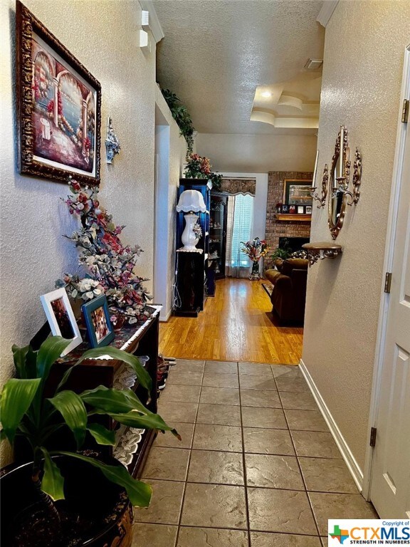 4305 Foster Ln, Killeen, TX 76549 - hallway featuring a textured ceiling, a textured wall, tile patterned flooring, baseboards, and a raised ceiling